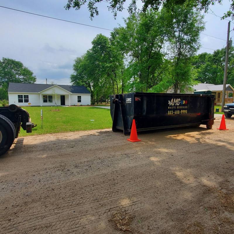 A roll-off dumpster set in a homeowner's driveway with a cone out front