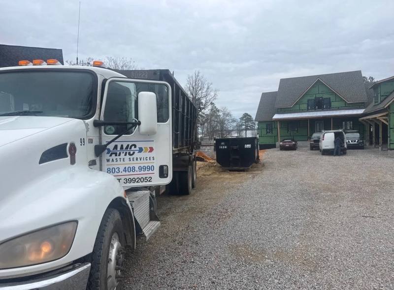 An AMC Waste Services truck delivering a roll-off dumpster on a custom home build