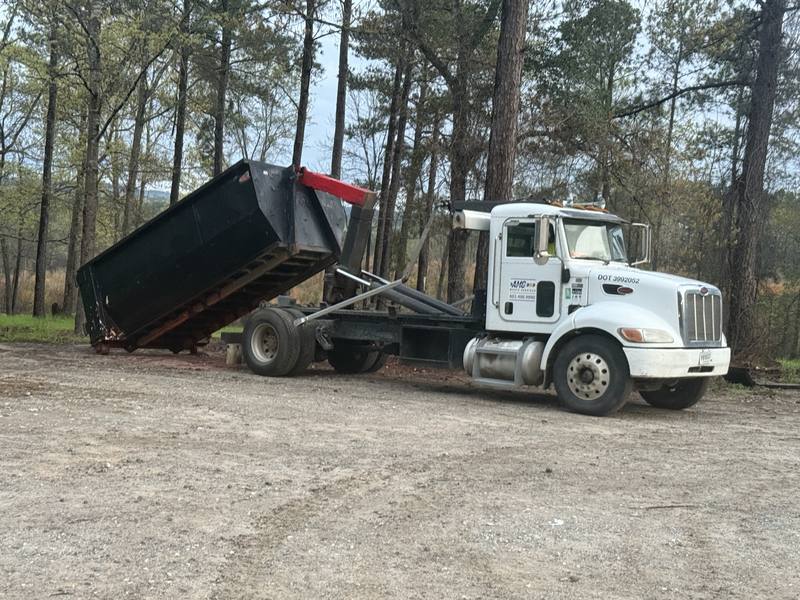 An AMC Waste Services truck tipping a 30 yard dumpster into place