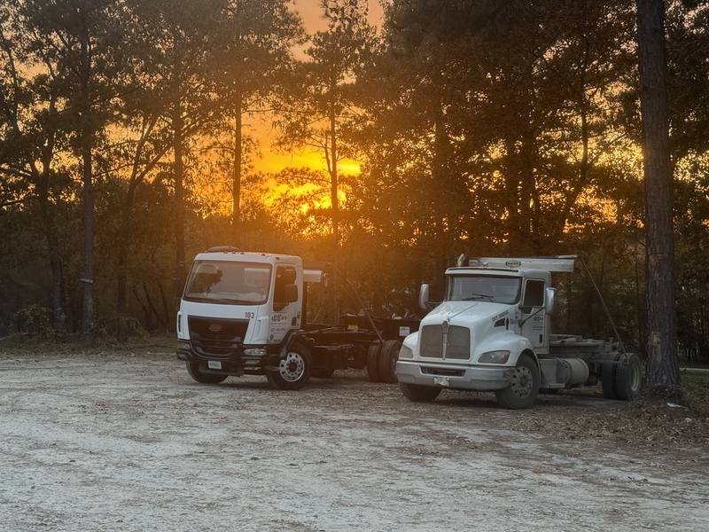 Two AMC Waste Services trucks parked at the yard at sunset